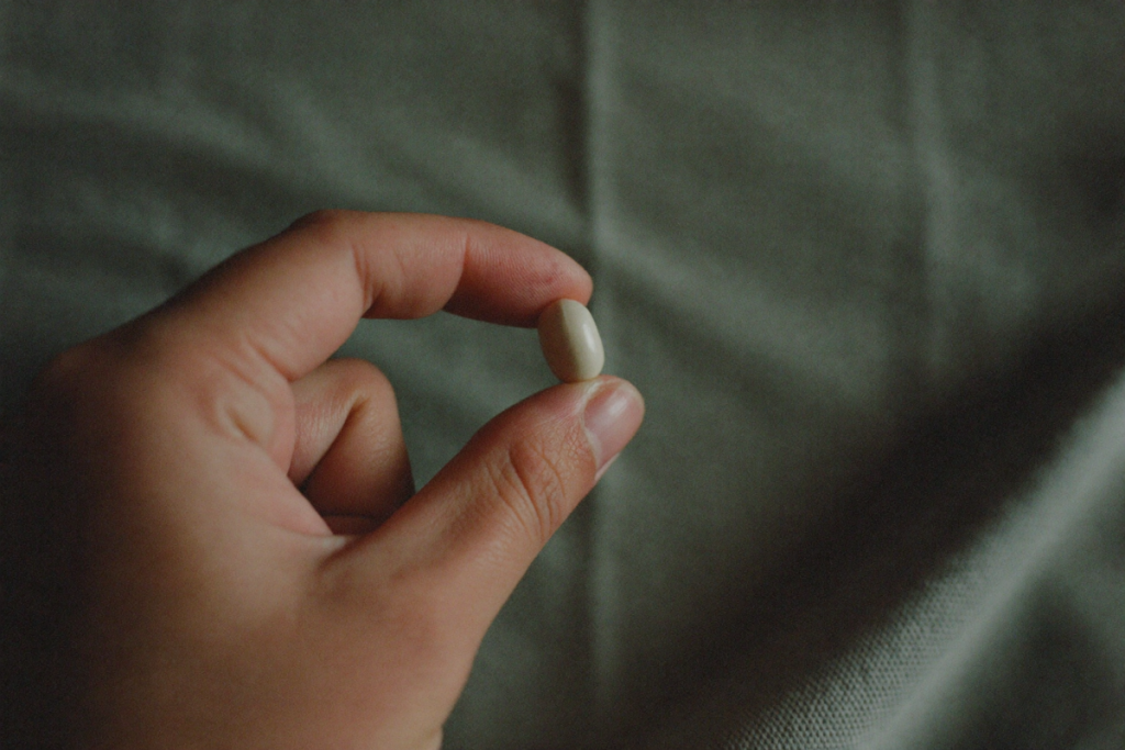 A single small white oral tablet resting on neutral linen in soft light
