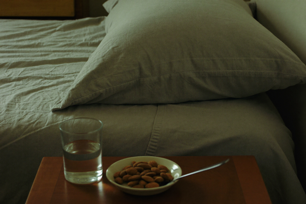 Early-morning bedroom scene with rumpled sheets, a water glass, and almonds on a wooden nightstand
