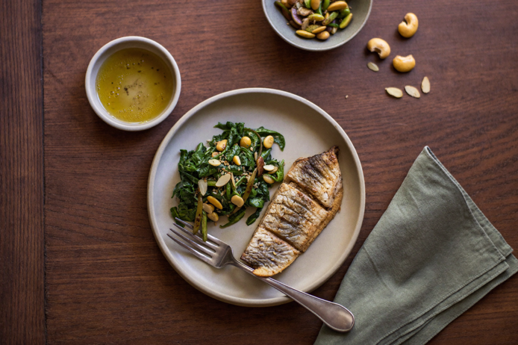 Overhead view of a balanced plate with fatty fish, greens, nuts, seeds, and legumes on a wooden table
