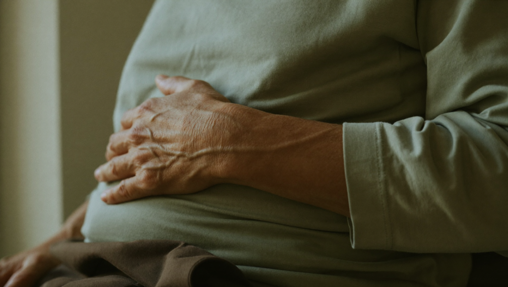 A calm person resting a hand near the liver area in soft natural light