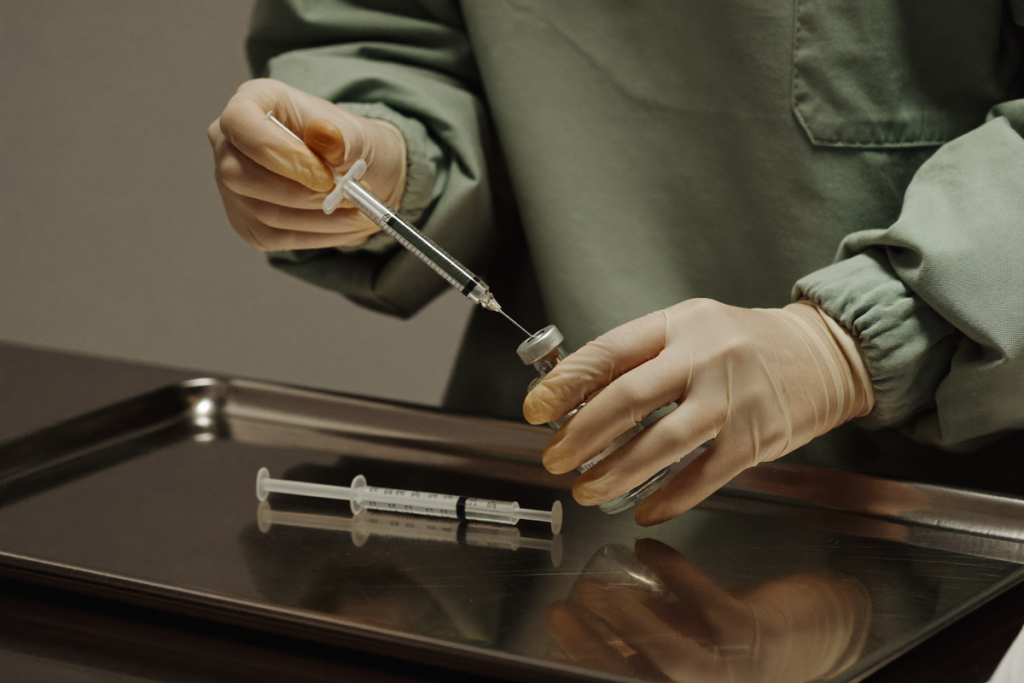 Gloved hands preparing a sterile vial and syringe on a clinical tray