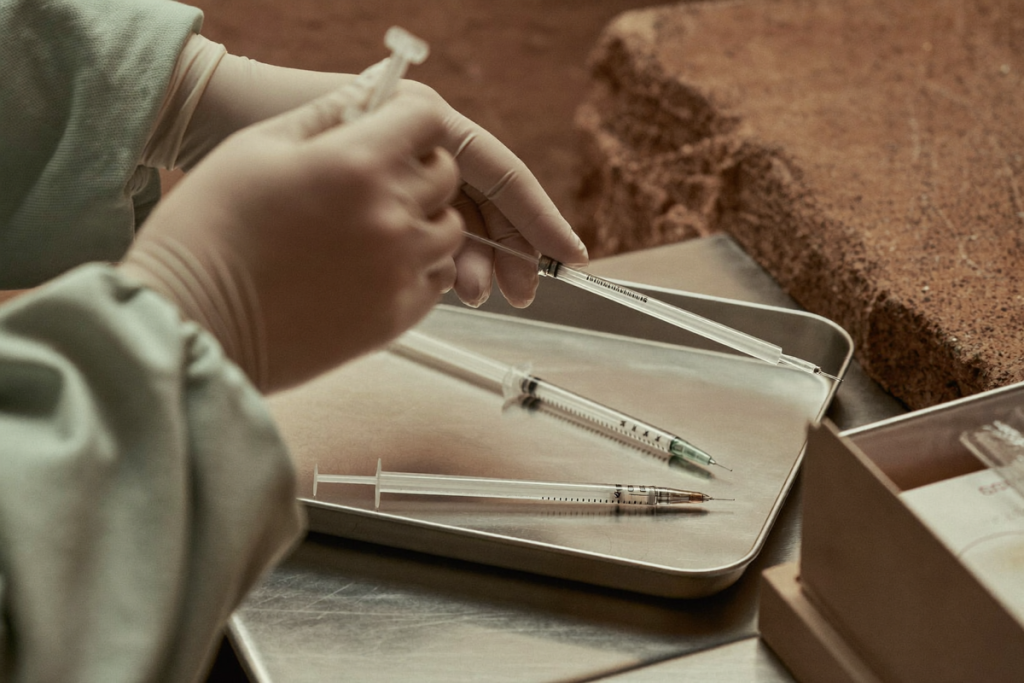 Gloved hands preparing a sterile syringe on a stainless tray, illustrating supervised injectable preparation