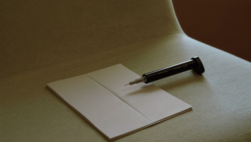 An unbranded weekly injection pen on a sage-green linen surface in soft natural light
