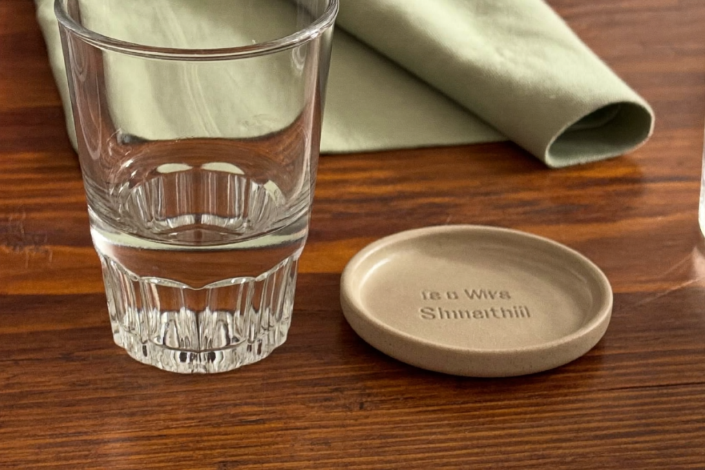A glass of water and a plain dish on a wooden table in soft morning light