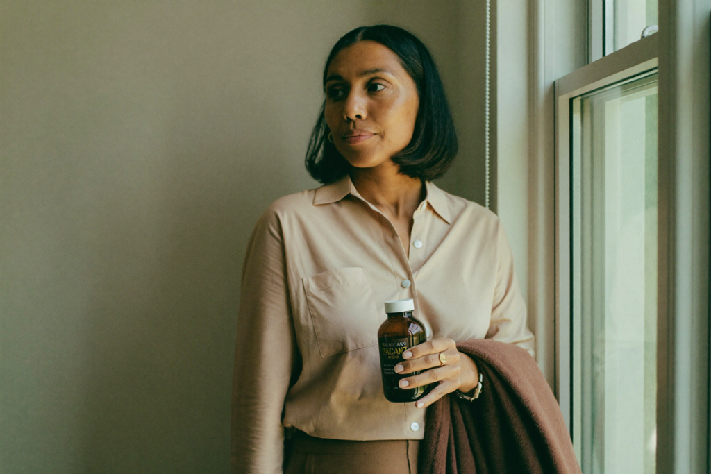 Woman reading the label on a supplement bottle by a window in soft natural light