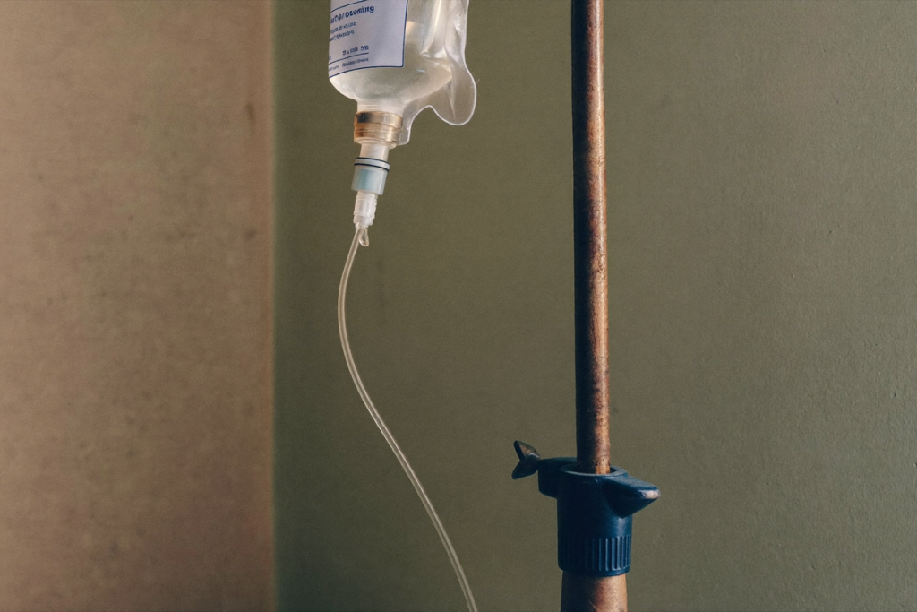 An IV drip line and clear saline bag on a stand against a soft sage-green background