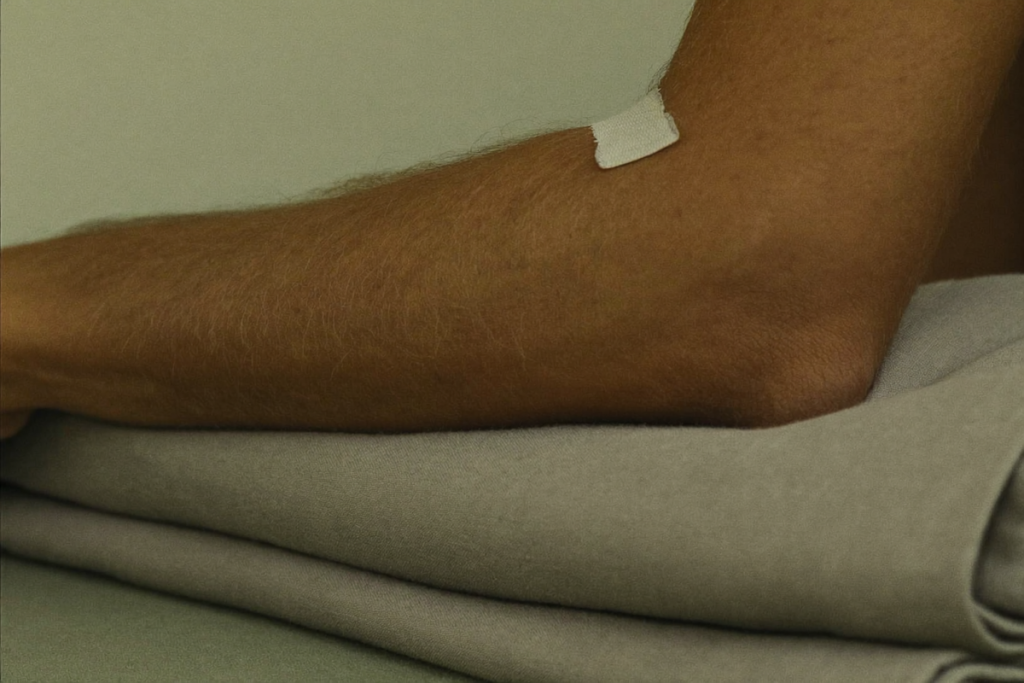 A calm forearm resting on folded cloth with a small bandage in soft natural light