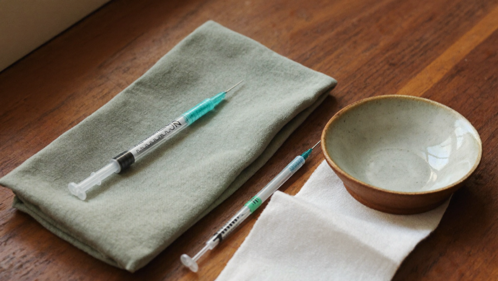Unbranded subcutaneous injection pen on a sage-green cloth beside an alcohol swab, illustrating semaglutide injection-site preparation