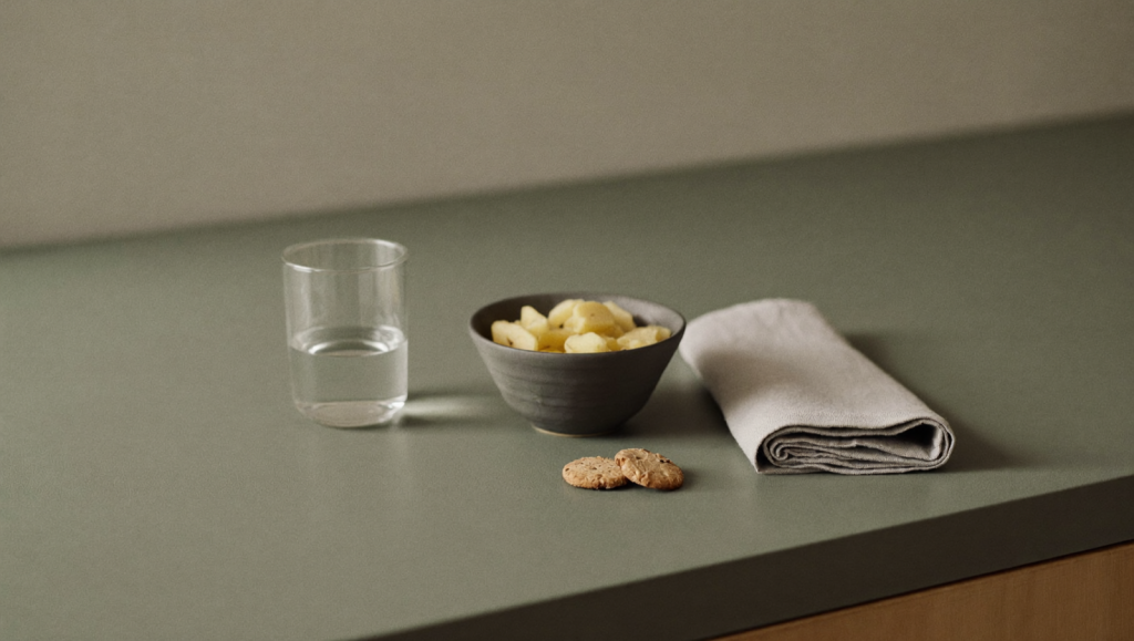 A glass of water, ginger, and plain crackers on a calm kitchen counter suggesting gentle relief from mild nausea