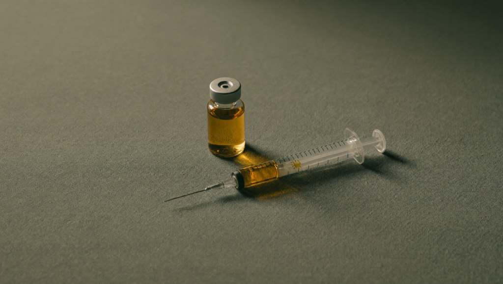 A small amber vial and syringe on a sage-green cloth in soft natural light