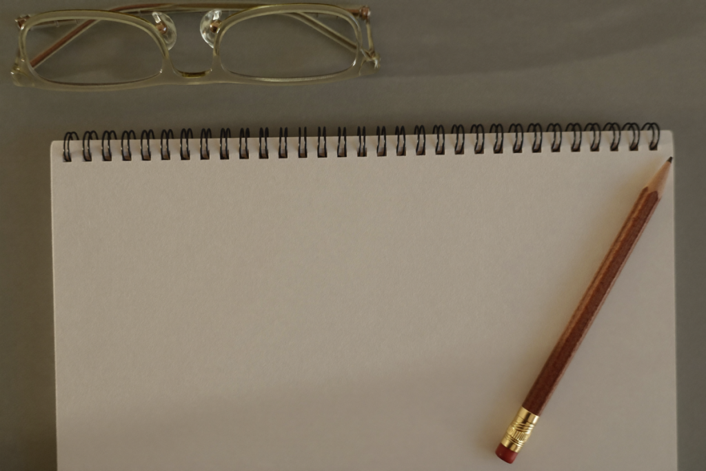 Blank notebook, pencil, and reading glasses on a sage-green desk suggesting careful review of evidence