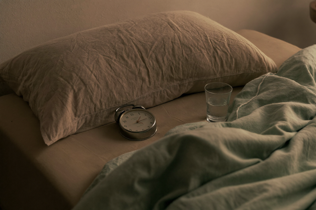 A bedside scene with a linen pillow, simple clock, and glass of water in warm afternoon light