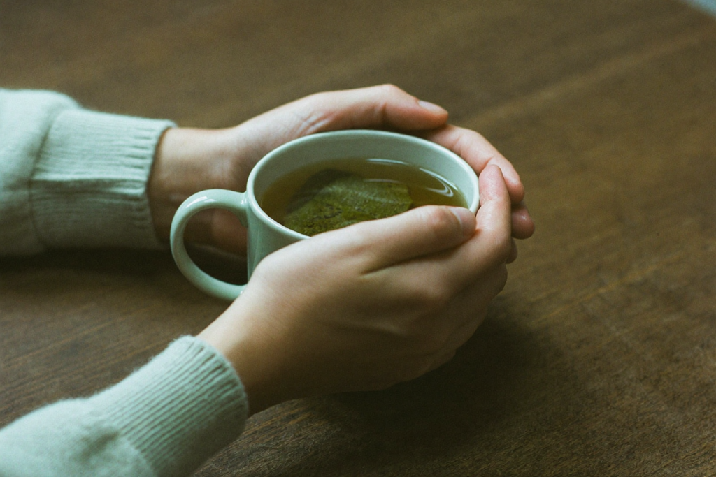 Hands holding a warm mug of tea at a table, suggesting management of mild digestive side effects