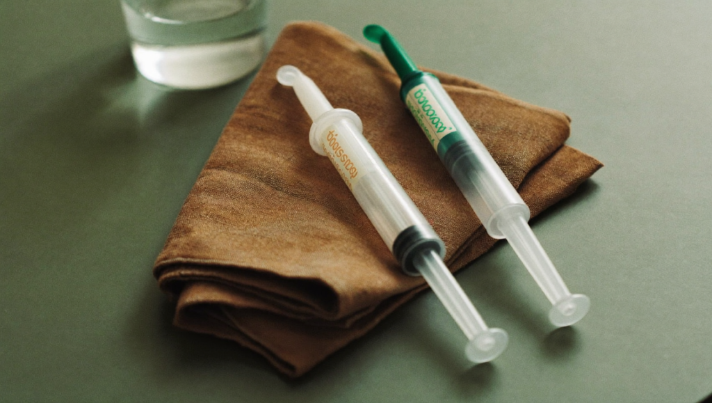 Two unbranded injectable pens side by side on a sage-green surface, representing a comparison of tirzepatide and semaglutide