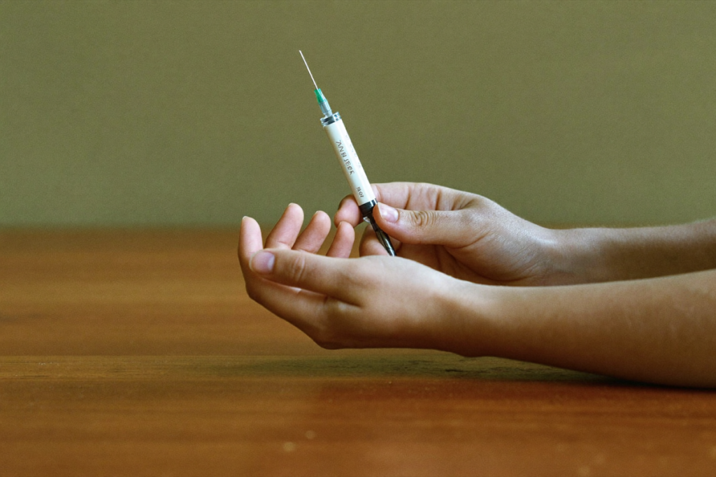 Hands holding a plain injection pen, illustrating once-weekly GLP-1 and dual-agonist dosing