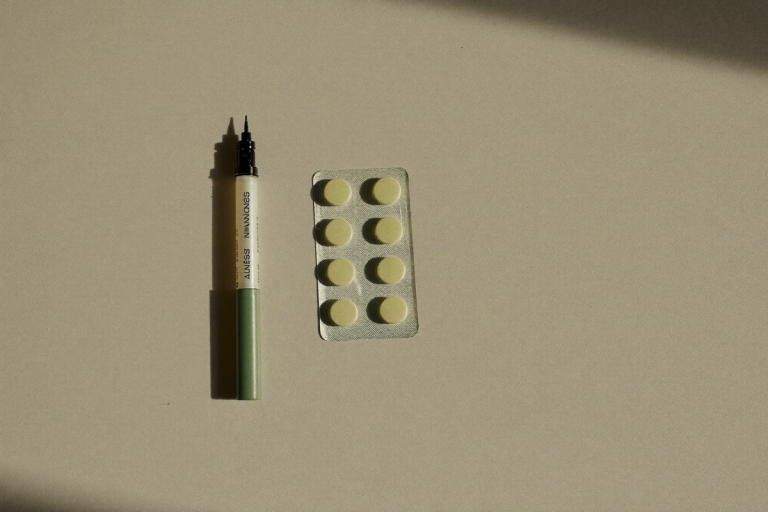 An unbranded autoinjector pen beside a blister pack of tablets on a neutral surface, illustrating PT-141 vs Viagra as two treatment forms